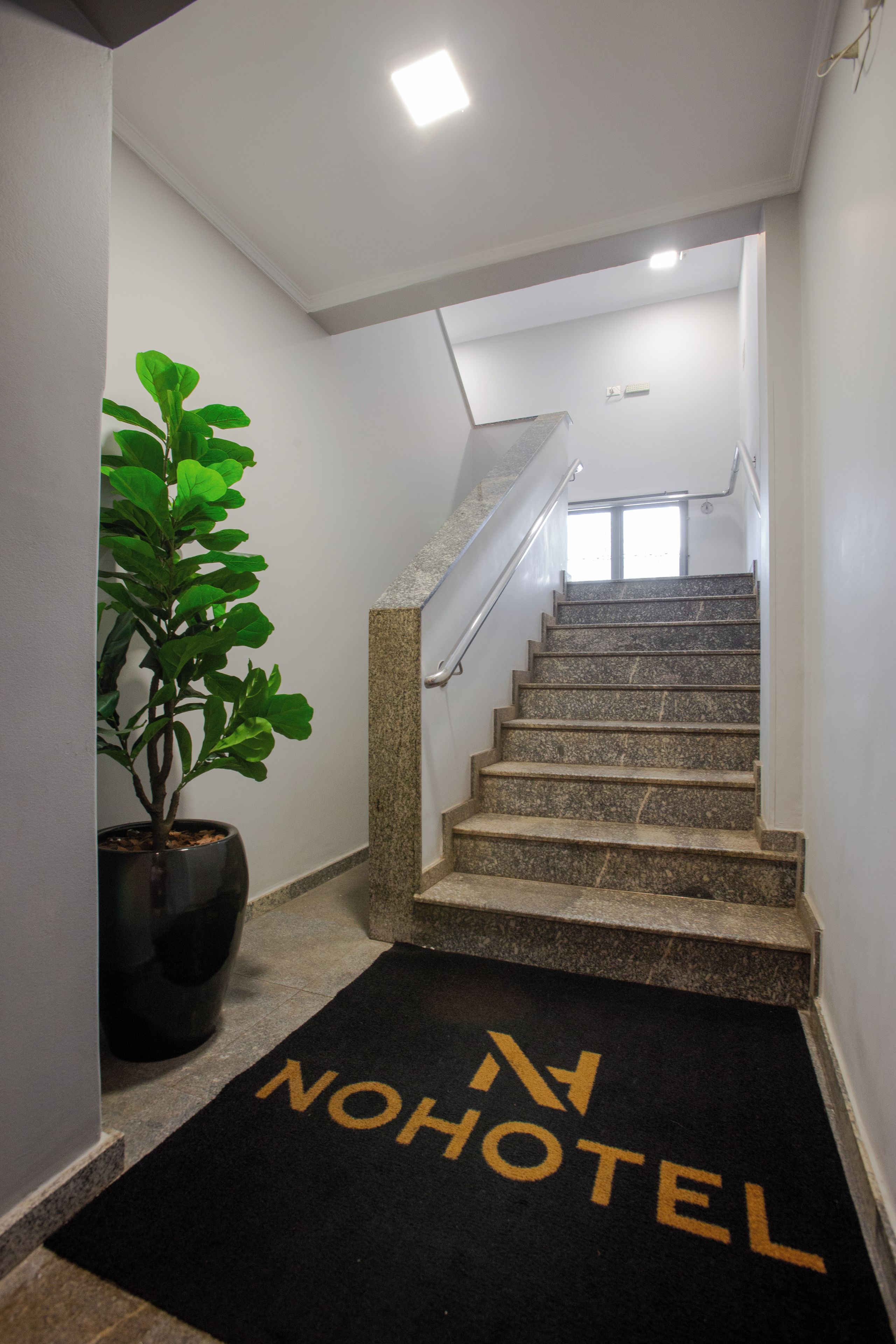 Una escalera con barandilla, una planta en maceta y un felpudo negro con la inscripción 'NOHOTEL'.