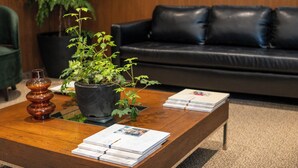 Una sala de estar con un sofá de cuero negro, una mesa de centro de madera con revistas, una planta en maceta y un jarrón decorativo.