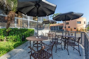 An outdoor patio with metal tables and chairs, umbrellas, and a chain-link fence. - Nohotel Nova Odessa (Nova Odessa)