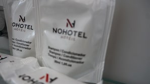 Dos bolsas blancas con la etiqueta 'NOHOTEL' que muestran indicaciones de contener champú y acondicionador.