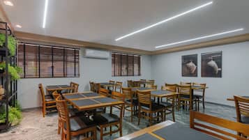A conference room with multiple tables and chairs, air conditioning units, and windows with blinds.