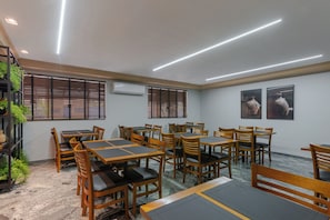 Une salle de conférence équipée de plusieurs tables et chaises, de climatiseurs et de fenêtres avec stores.