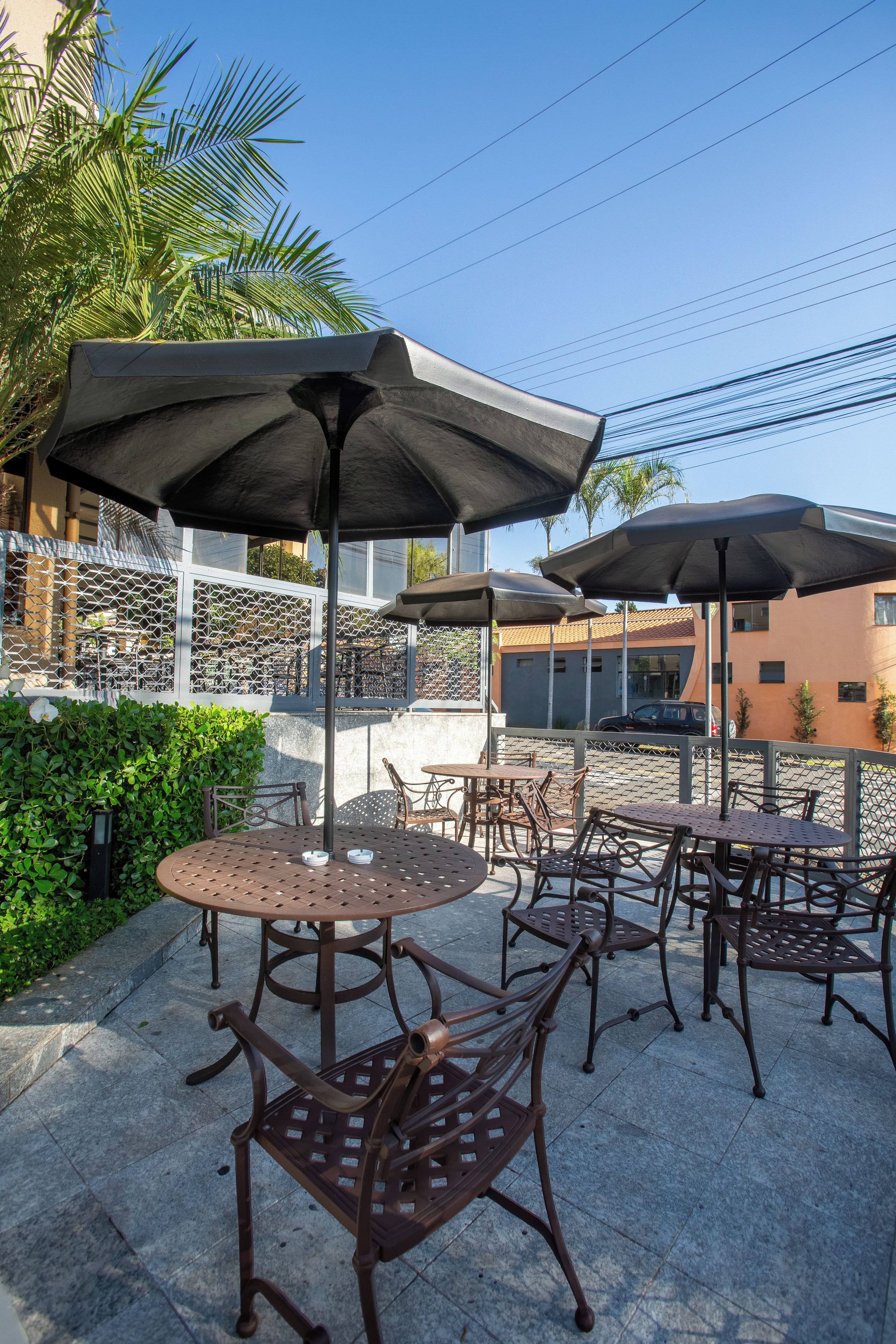 Mobiliario exterior en terraza con mesas y sillas, sombrillas y una valla decorativa.