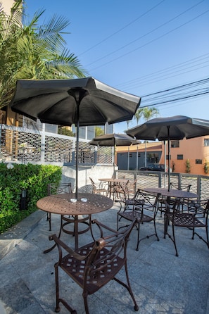 Mobiliario exterior en terraza con mesas y sillas, sombrillas y una valla decorativa.
