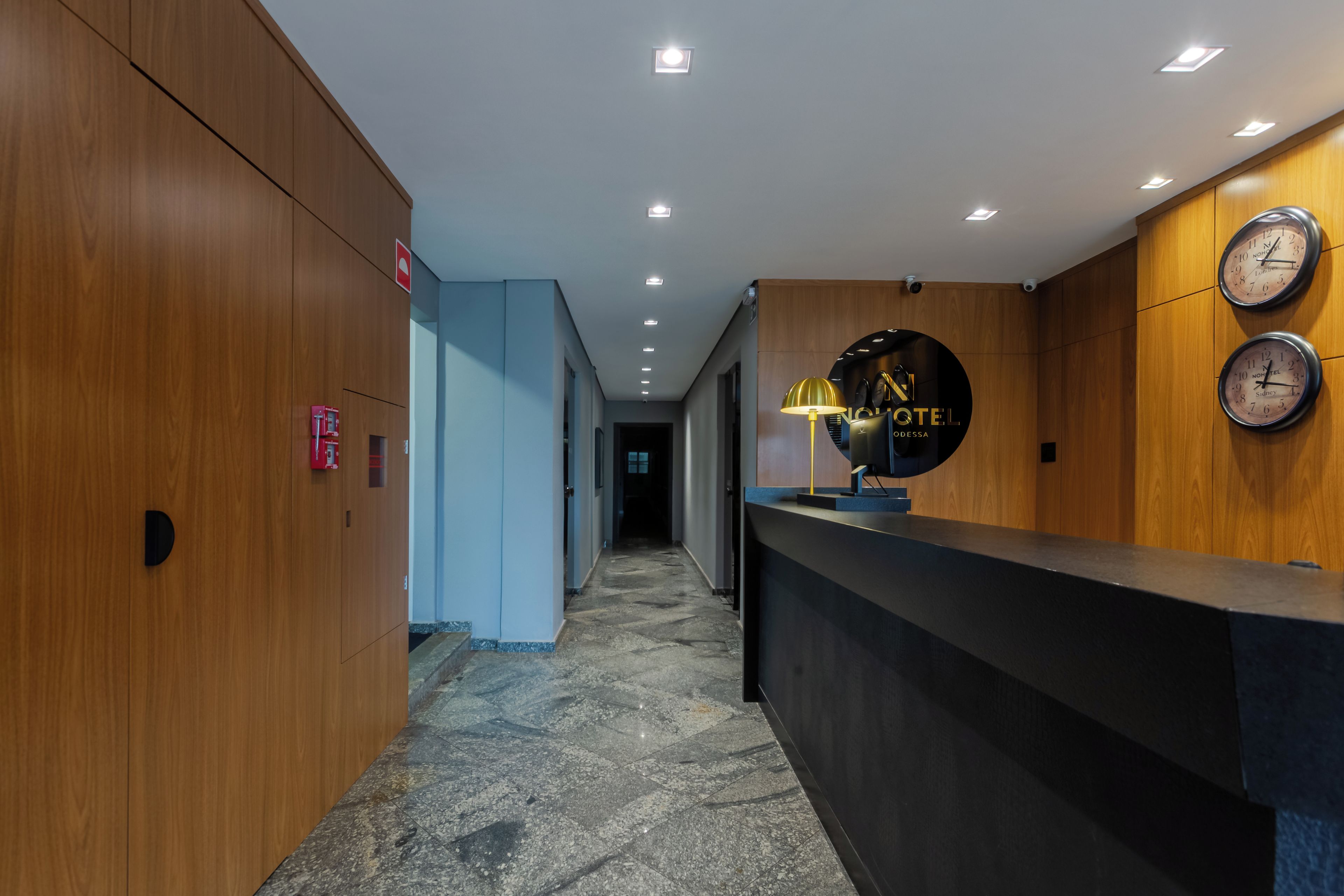 A hotel reception area with a wooden reception desk, a black clock, and a sign that reads 'NO HOTEL'.