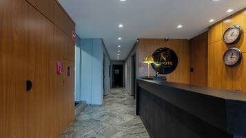 A hotel reception area with a wooden reception desk, a black clock, and a sign that reads 'NO HOTEL'.