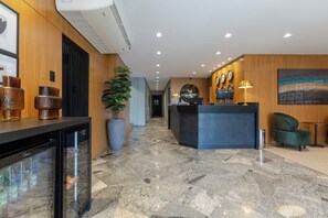 Un hall d’hôtel avec un comptoir d’accueil, une grande plante en pot et une horloge murale.