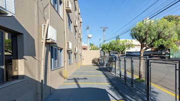 A parking area with a building on one side, a fence on the other, and trees in the background.