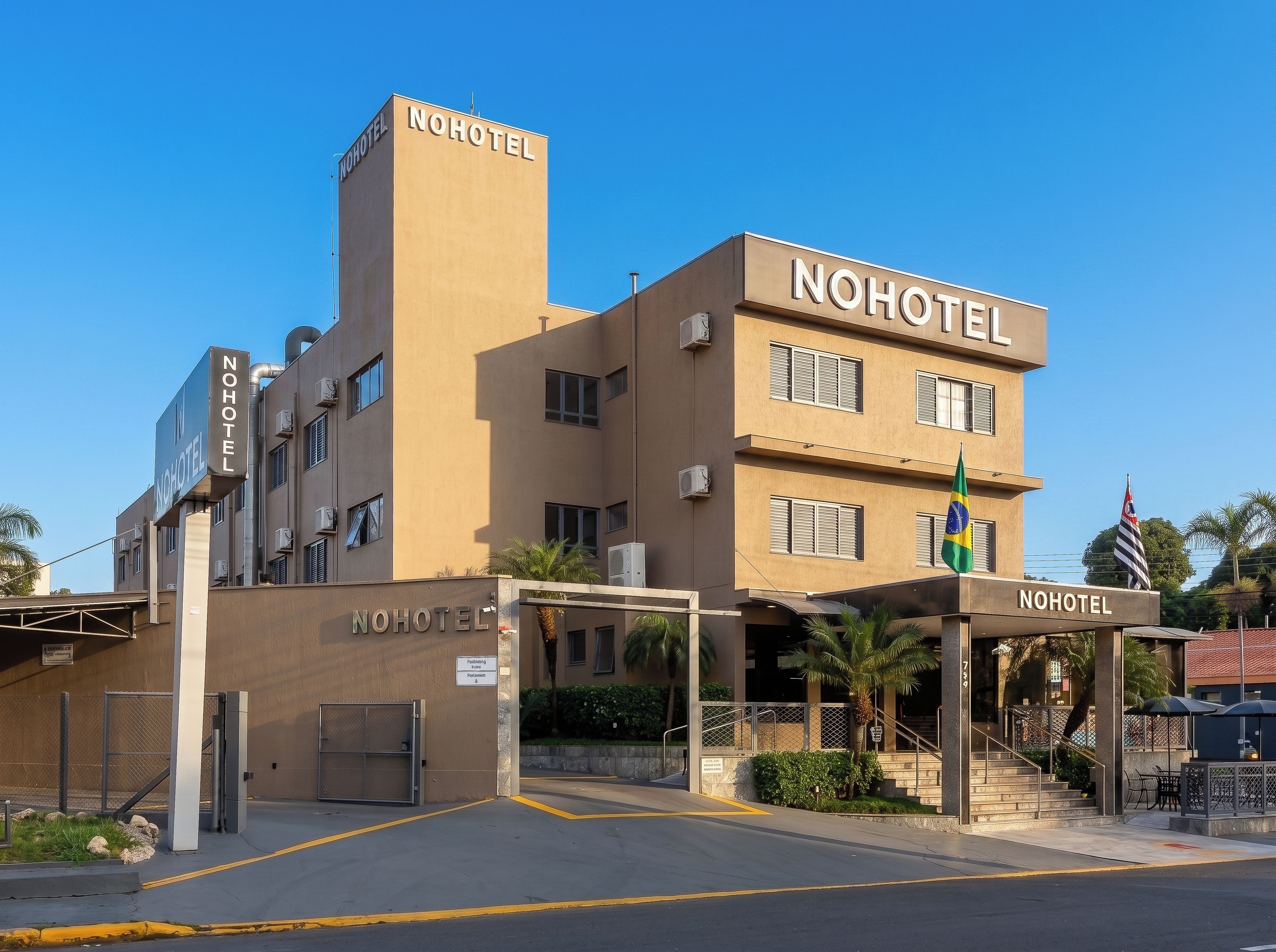 Um edifício de vários andares com a sinalização 'NOHOTEL', área de estacionamento e um mastro com bandeiras.