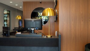 Mostrador de recepción de hotel con una computadora, una lámpara de escritorio y un espejo que refleja el nombre del hotel.