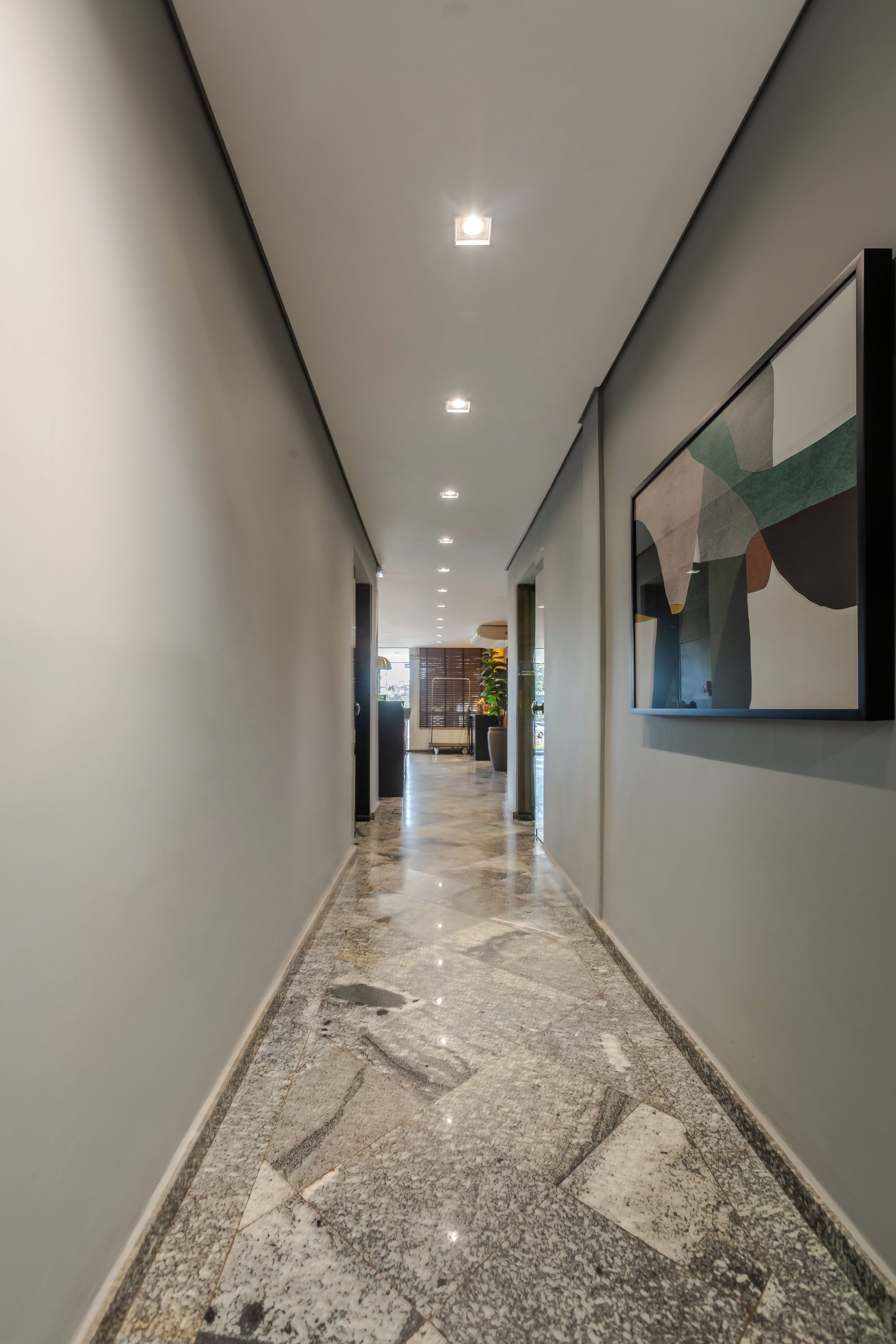 Un couloir doté d’un sol en marbre poli, de luminaires encastrés au plafond et d’un tableau abstrait encadré accroché au mur.