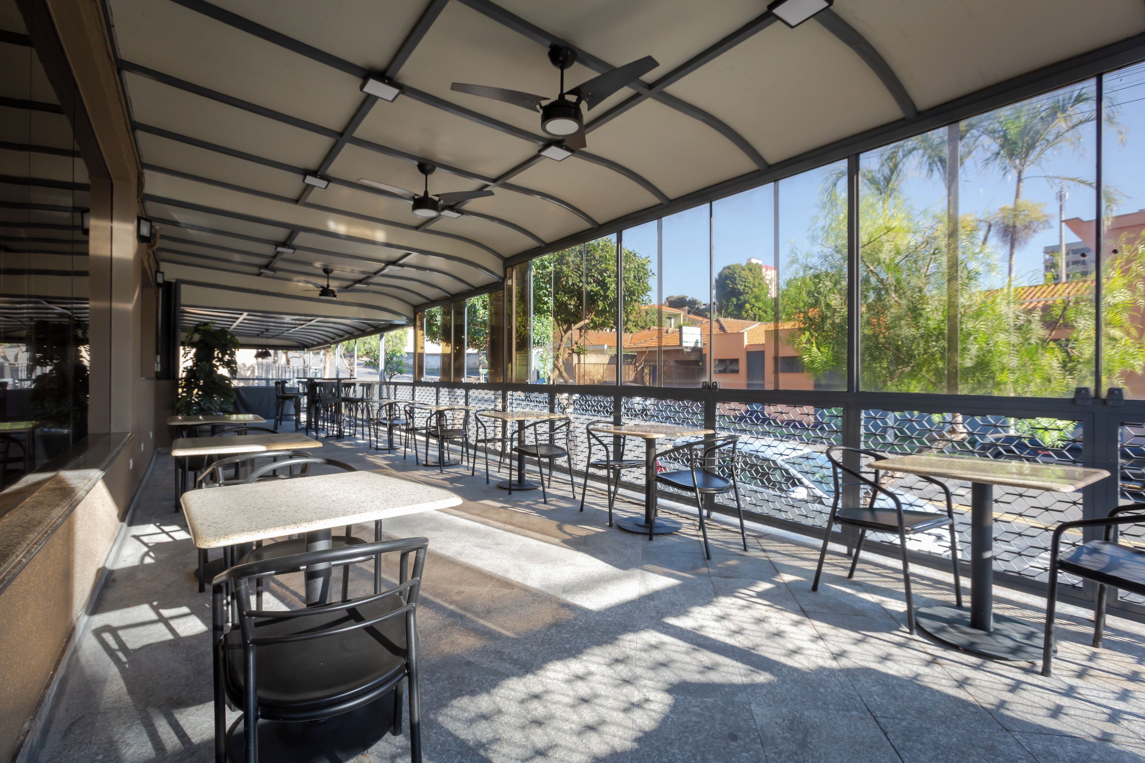 An outdoor seating area with tables and chairs, a covered roof, and a view of the river and buildings.