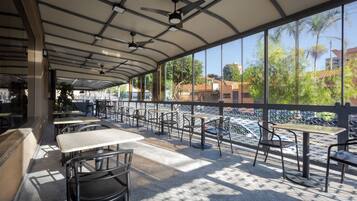 An outdoor seating area with tables and chairs, a covered roof, and a view of the river and buildings.