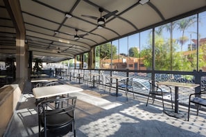 Un espace extérieur aménagé avec des tables et des chaises, un toit abrité et une vue sur la rivière et les bâtiments.