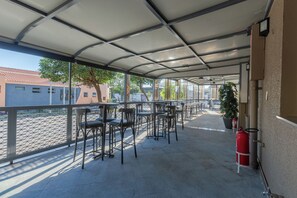 Un espacio de estar al aire libre cubierto, con mesas y sillas, un extintor y vista a la calle.