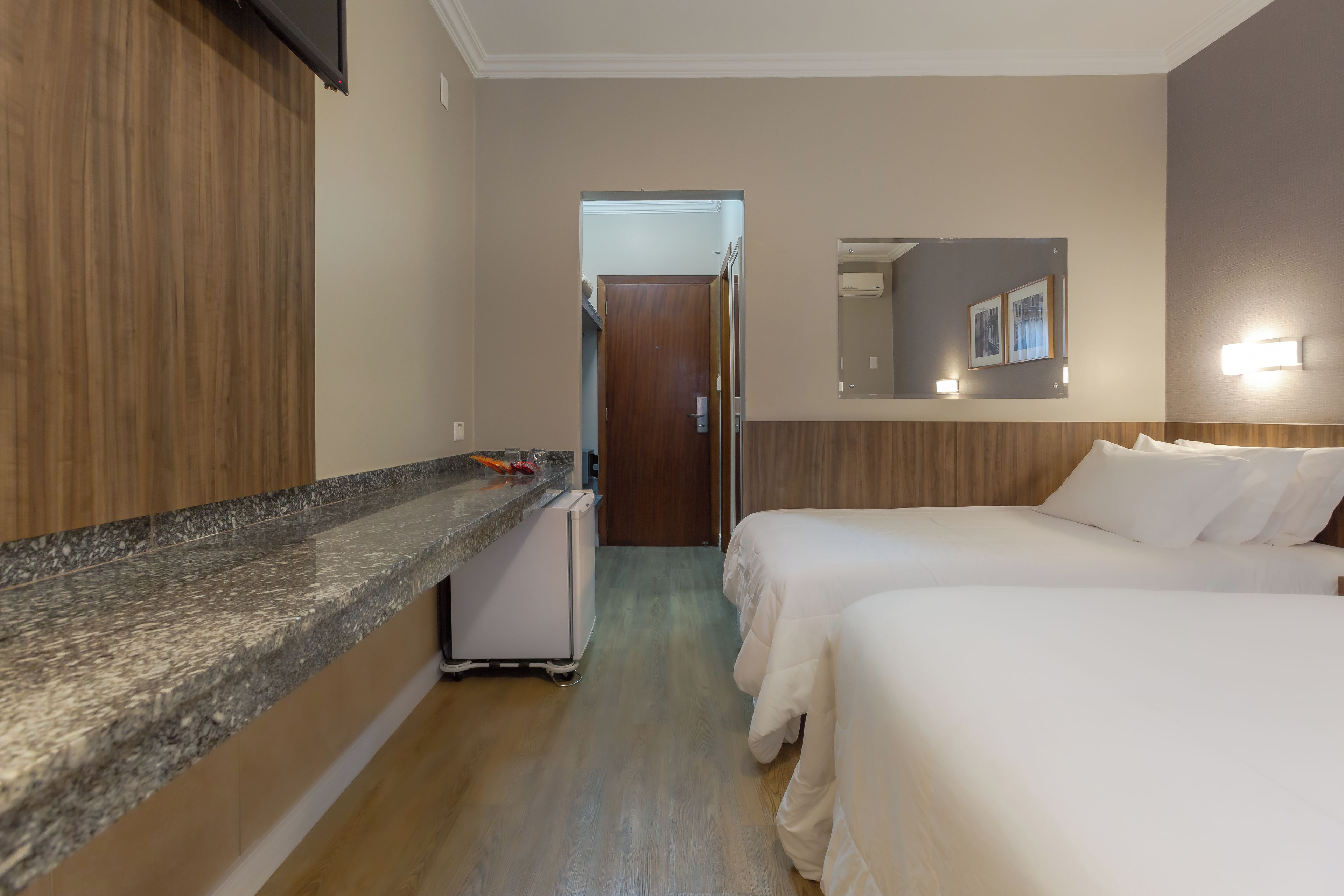A hotel room with a kitchenette, a bed, a bedside table, and a mirror.