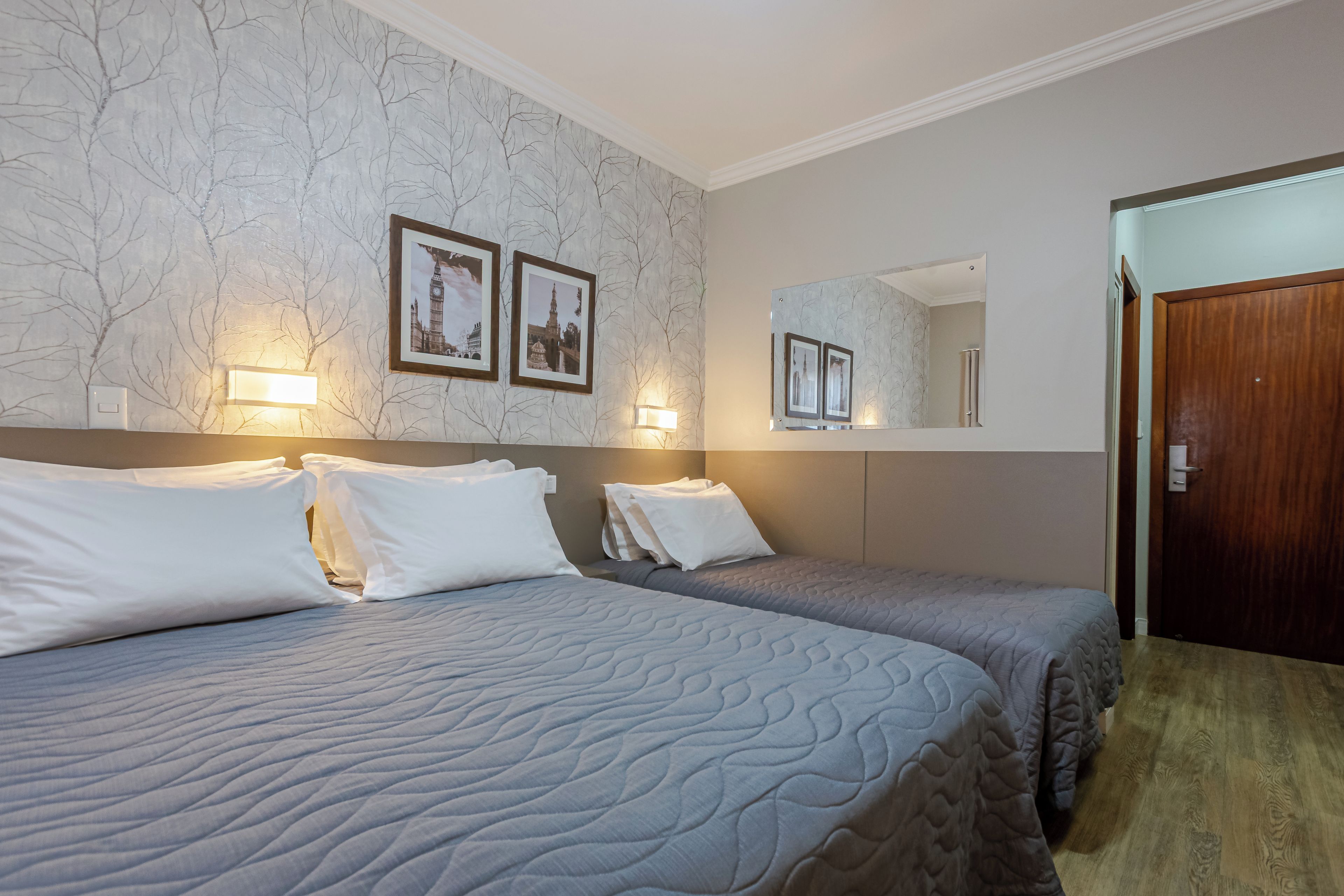 A hotel room with two beds, a large mirror, and wall-mounted picture frames.
