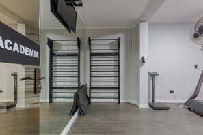 Ein Fitnessraum mit zwei Klimmzugstangen, einem Laufband und einem an der Wand montierten Fernseher.