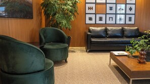 Une pièce comprenant un fauteuil vert foncé, un canapé en cuir noir, un mur en bois orné de tableaux encadrés et une plante en pot.