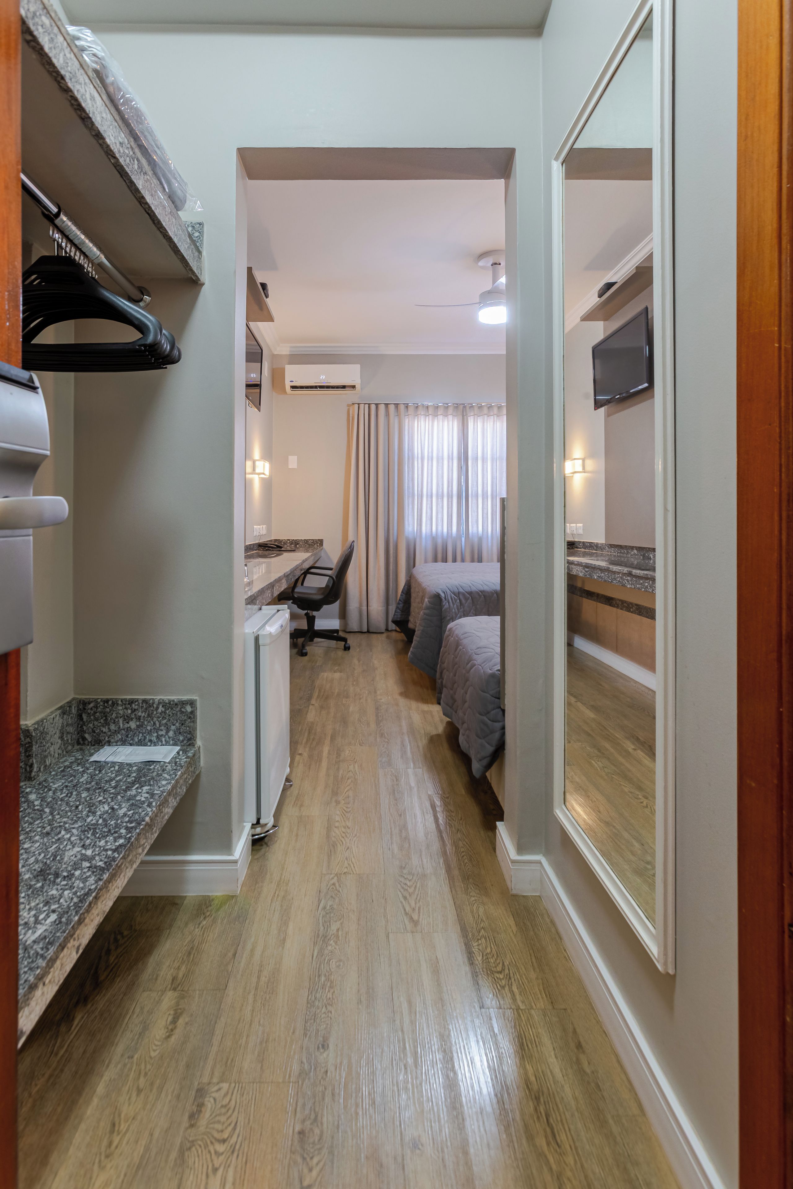 A narrow hallway leading to a bedroom with a bed, a desk, and a chair.