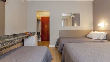 A hotel room with two beds, a small kitchenette, a mirror, and a door leading to another room.