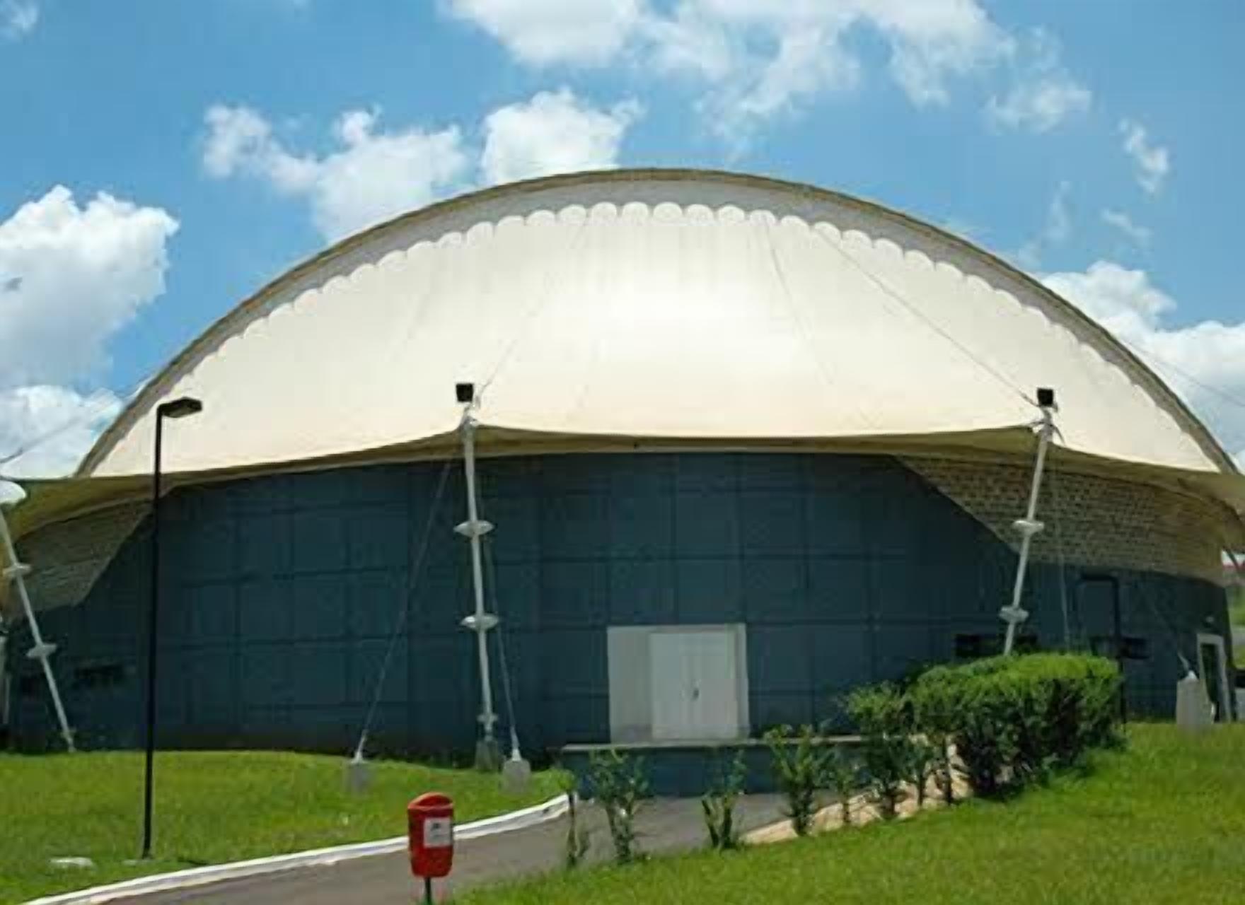 A large, dome-shaped building with a flat roof, surrounded by a grassy area and a few small bushes.
