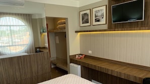 Een compacte hotelkamer met een bed, een klein bureau, een televisie en een raam met gordijnen.