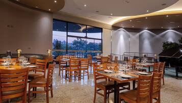 A restaurant with multiple tables and chairs, large windows, and a piano.