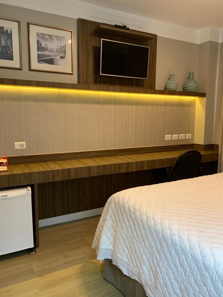 Une chambre d’hôtel avec un lit, un bureau, une télévision et des tableaux encadrés au mur.