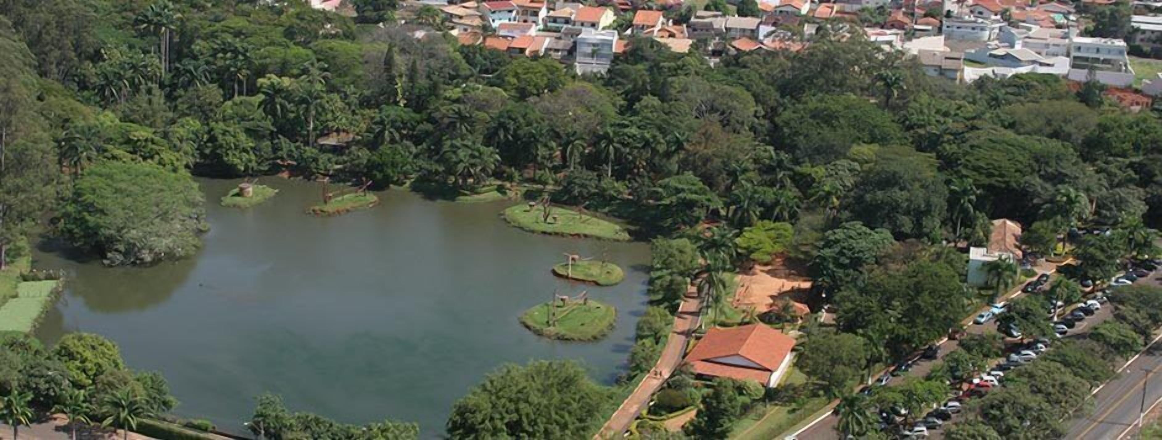 Vista aérea de um bairro residencial com um grande lago rodeado por vegetação exuberante e algumas casas.