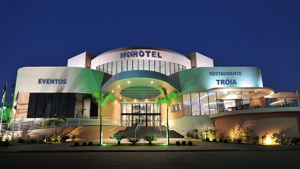 Een hotel met een modern design, voorzien van een centrale ingang met treden, een bord met 'EVENTOS' en een restaurant genaamd 'TRÓIA'.
