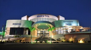 Een hotel met een modern design, voorzien van een centrale ingang met treden, een bord met 'EVENTOS' en een restaurant genaamd 'TRÓIA'.