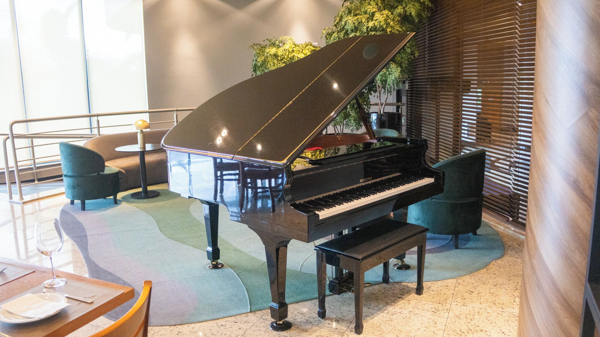 Un piano de cola en una habitación luminosa con un diseño moderno, que incluye un área de estar con sillas y una pequeña mesa.