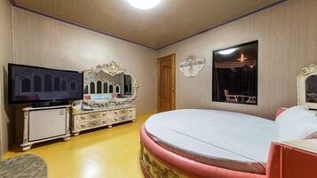 A bedroom with a large bed, a television, a dresser, and a mirror.