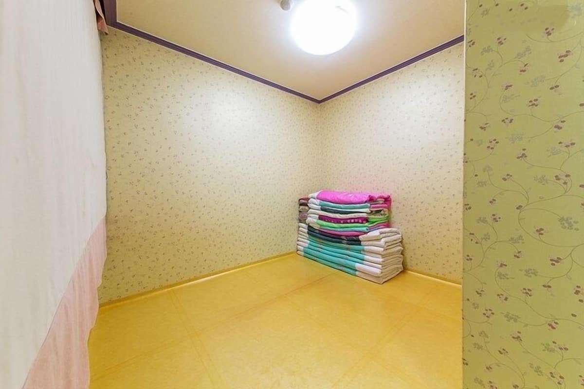 A corner room with a yellow floor, a stack of folded towels, and floral wallpaper.