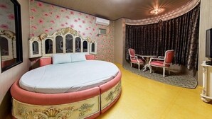 Une chambre à coucher avec un lit rond, une coiffeuse avec un miroir, une petite table et des chaises.