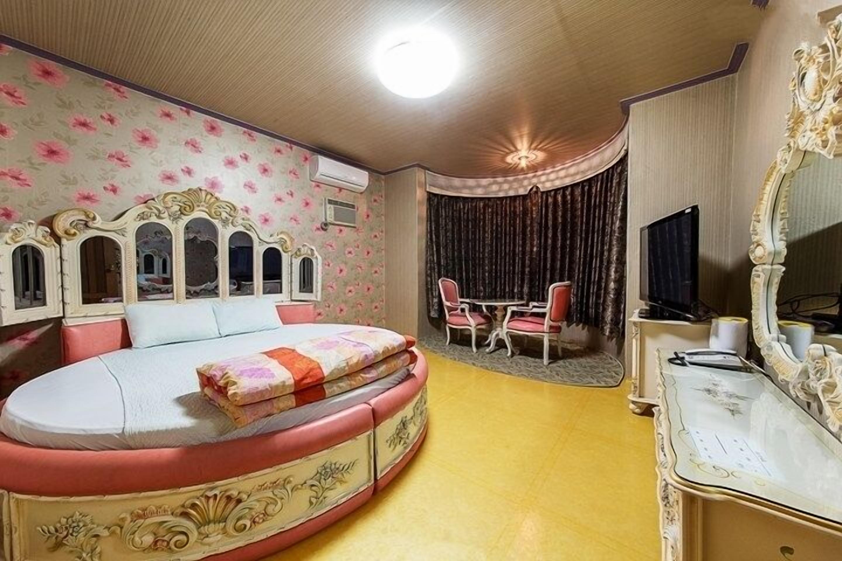 Ein Schlafzimmer mit einem großen Bett, einem Fernseher, einem Schreibtisch und einem Sessel.