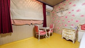 Une petite pièce avec une table ronde et deux chaises, un mur décoratif recouvert d’un papier peint à motifs floraux et un rideau rouge.