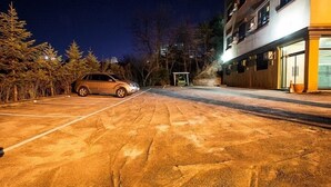 Un parking avec une voiture, des arbres et un bâtiment doté d’un garage.