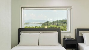 Une chambre d’hôtel avec un lit, une table de chevet, une télécommande et une fenêtre donnant sur une rivière et des montagnes.