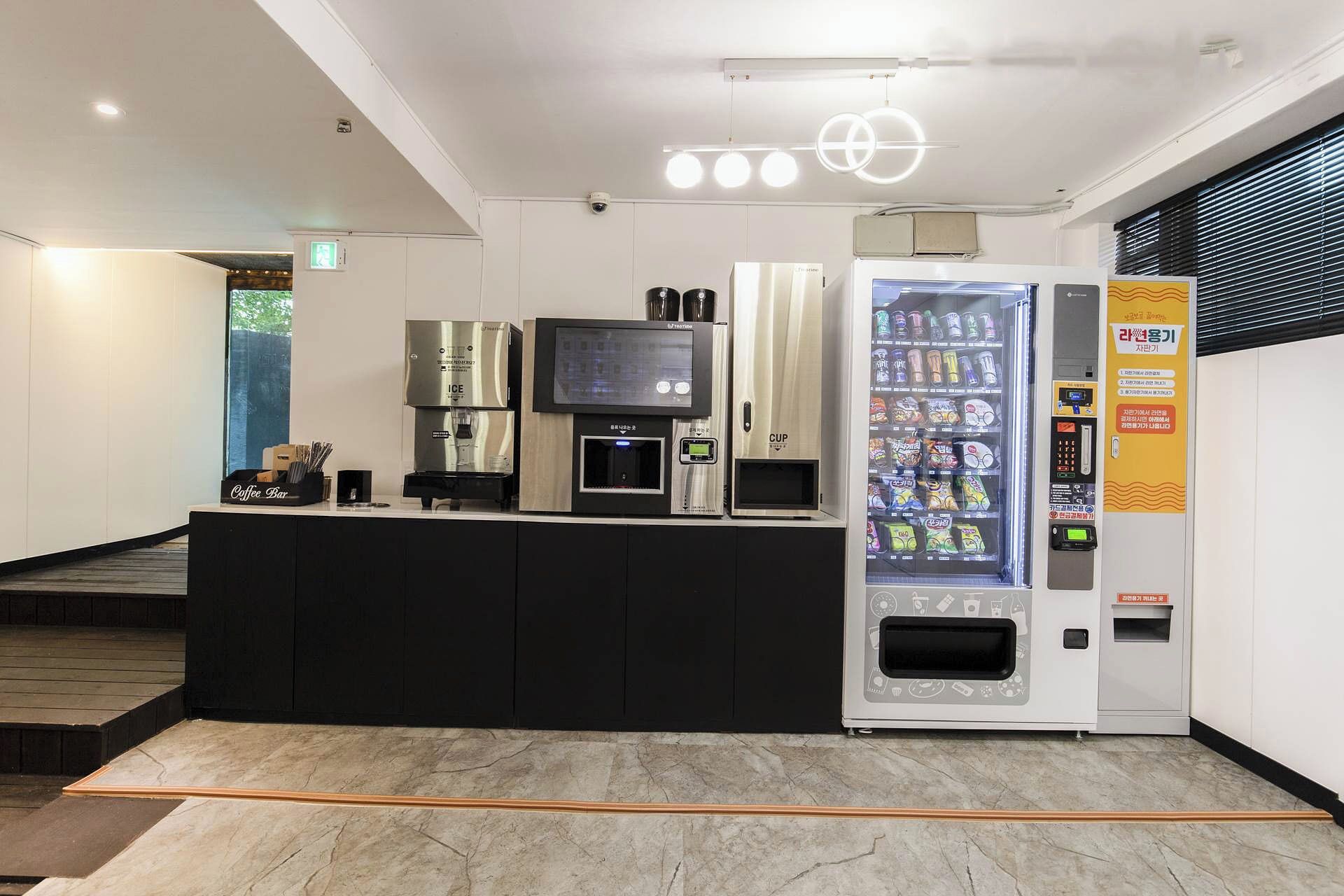 Un espace d’accueil moderne comprenant un bar à café, un distributeur automatique de boissons et un écran numérique.