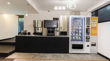 Un espace d’accueil moderne comprenant un bar à café, un distributeur automatique de boissons et un écran numérique.