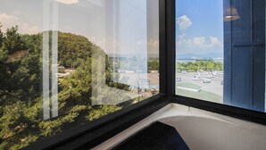 Une chambre d’hôtel dotée d’une grande fenêtre donnant sur un parking et un paysage vallonné.