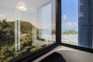 A hotel room with a large window overlooking a parking area and a hilly landscape.