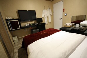 A hotel room with a bed, a desk with a computer, a TV, and a wardrobe.