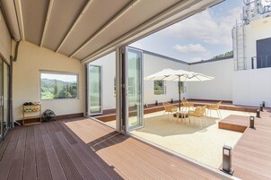 A spacious patio with a table and chairs, a fan, and a view of a mountainous landscape through large glass doors.