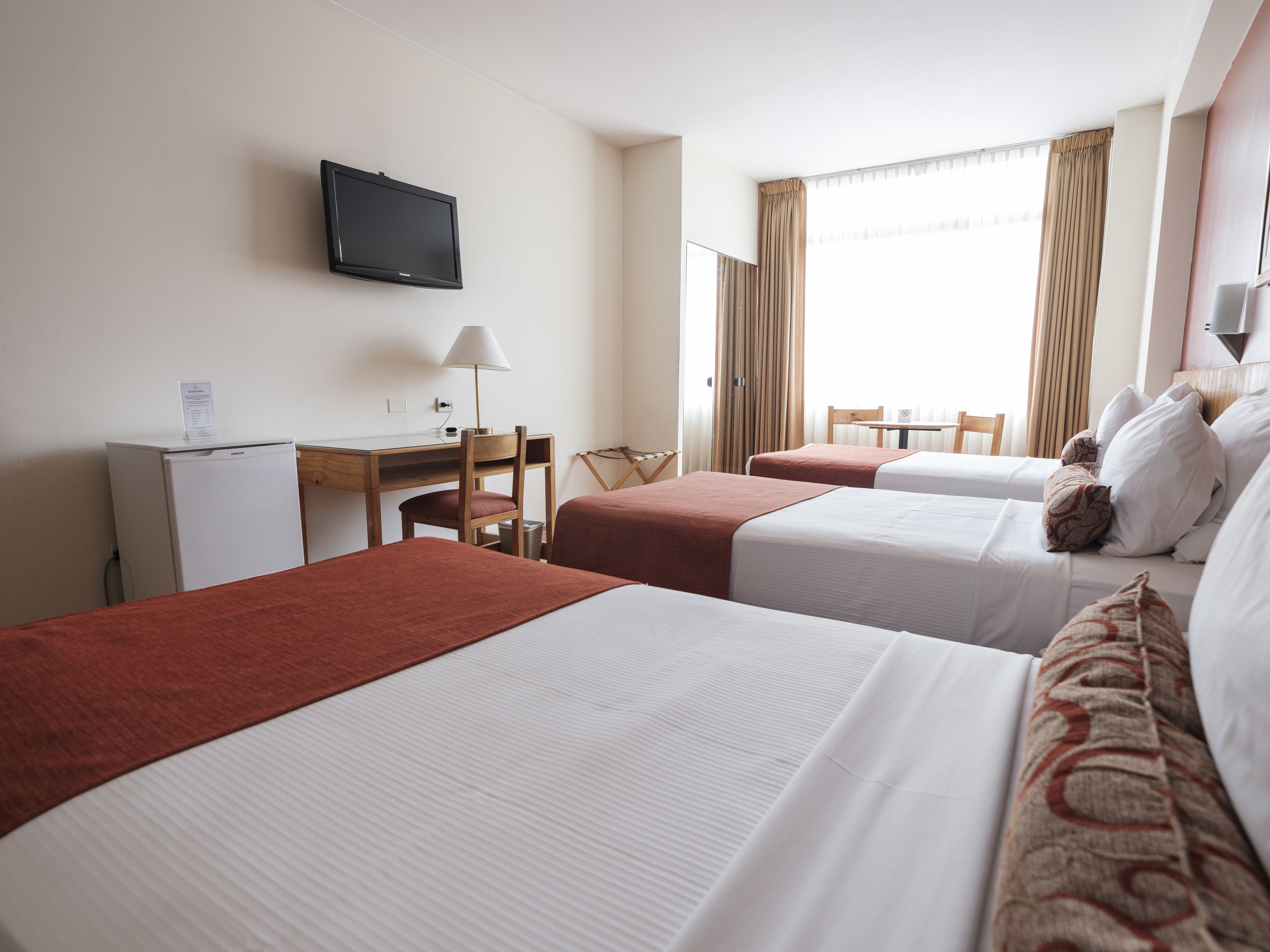 A hotel room with two beds, a desk, a chair, a TV, and a window with curtains.