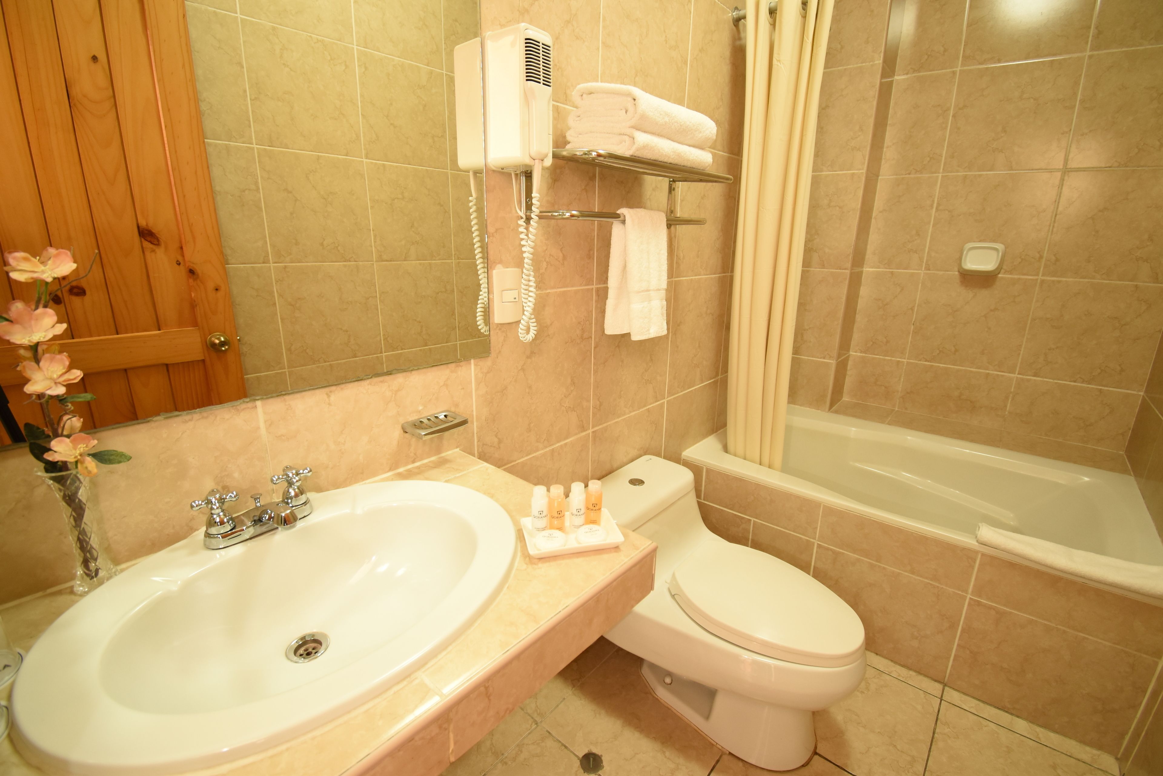 A bathroom with a sink, toilet, and bathtub. There is a towel rack with towels and a hairdryer on the wall.