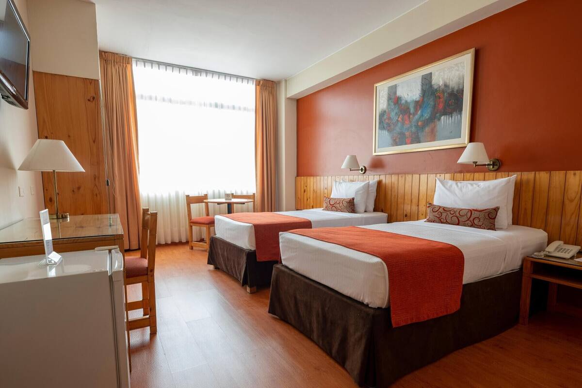 Habitación de hotel con dos camas, un escritorio, una silla, un televisor y un cuadro en la pared.