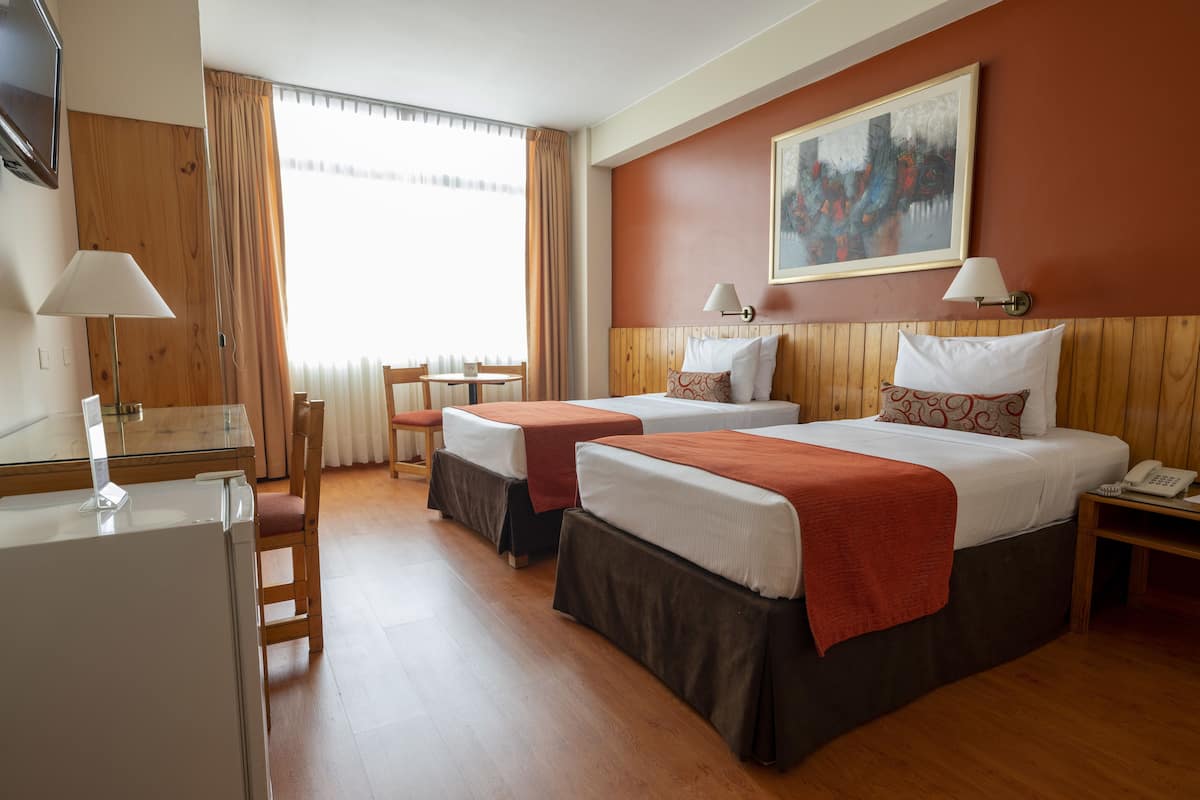Habitación de hotel con dos camas, un escritorio, una silla, un televisor y un cuadro en la pared.